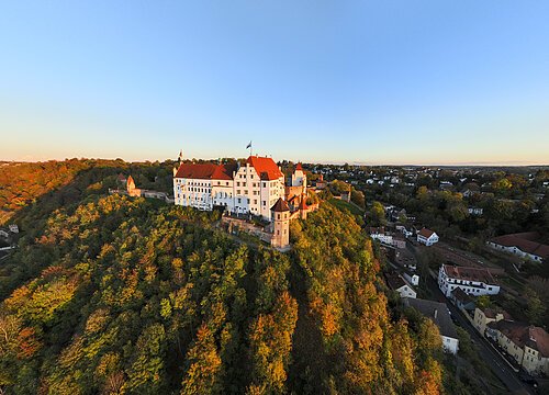 Burg auf bewaldetem Hügel mit umliegender Stadt bei klarem Himmel im Abendlicht